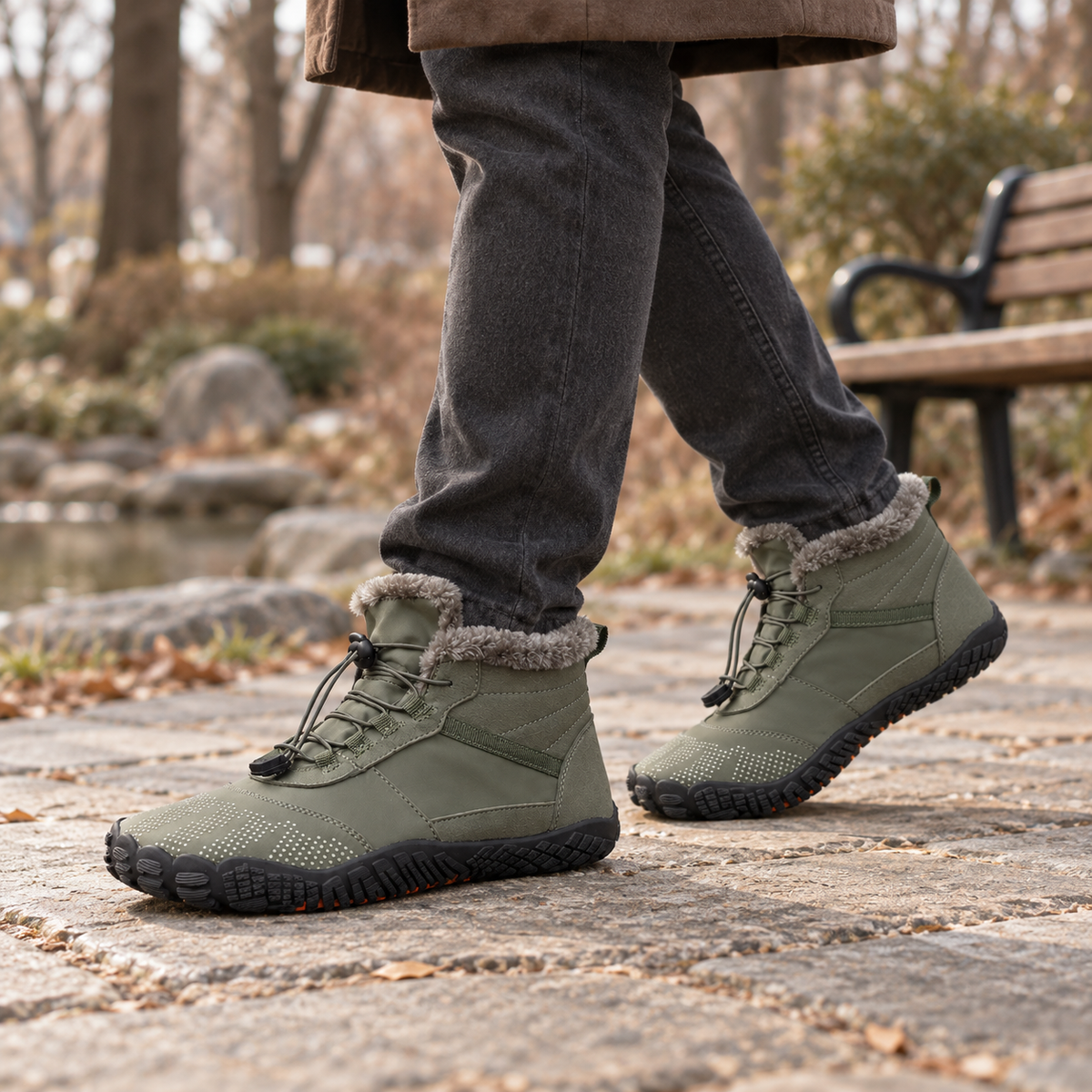Army green fleece-lined barefoot boots worn with casual trousers in a park setting.